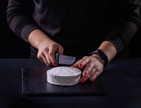 Girl slices goat brie cheese on a dark background.の写真素材