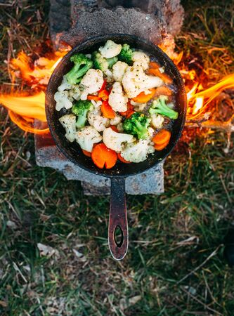 Cauliflower, broccoli and carrot in a pan. Cooking on an open fire. Outdoor food. Grilled vegetables. Food on a camping tripの写真素材