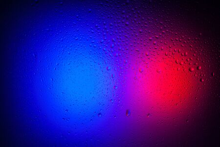 Drops of water on glass in red-blue neon light. Rain on the glass against the background of two colored lights. Abstract photo for backgroundの写真素材