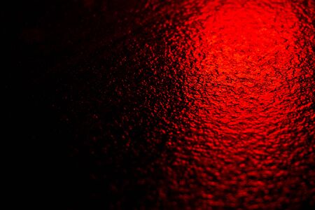Abstract photo reflection of light on a wet surface. Red neon light on a textured wet surface. Reflection of lights on the pavementの写真素材
