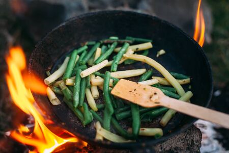 String beans in a pan. Cooking vegetables on an open fire. Food on a camping trip. Wooden spatula in a panの写真素材