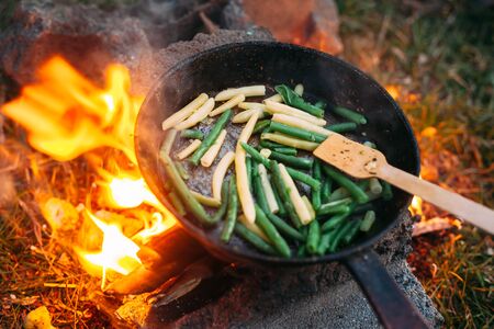 String beans in a pan. Cooking vegetables on an open fire. Food on a camping trip. Wooden spatula in a panの写真素材