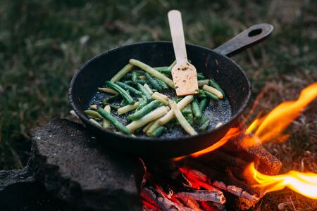 String beans in a pan. Cooking vegetables on an open fire. Food on a camping trip. Wooden spatula in a panの写真素材
