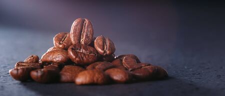 Grains of black coffee on a black granite countertop with yellow light from behind. Advertising photo of coffee. Photo with a glare from the light. Back light on a pyramid with grains.の写真素材