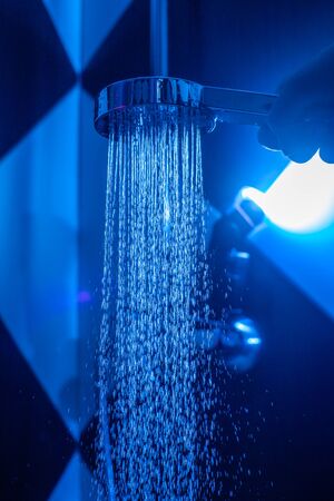 Girl holds a watering can in a shower cabin with blue backlight. Falling drops of water from a...