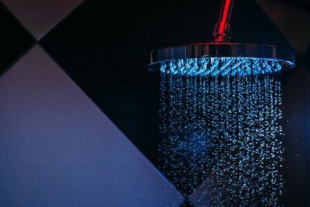 Drops of water fall from a watering can in the shower in blue light. Water drops close-up. Flow of water. Big round watering can.の写真素材