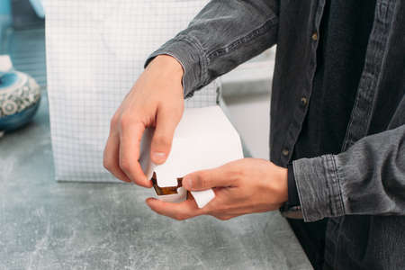 A guy in a gray shirt opens a paper box with a vegan burger. A food package with a food delivery in the background.の写真素材