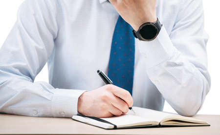 A business man writes with a pen in a black notebook while sitting at a table. The guy holds on to...