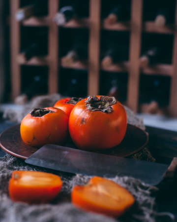Persimmon on a plate and wood surface. Background with wine bottles.