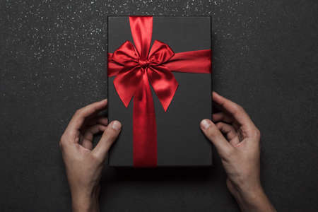 Hands holding a black gift box with a red bow on a black granite background.の写真素材