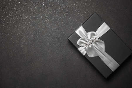 Black gift box with a silver ribbon and a large bow on a granite dark background. Place for the inscriptionの写真素材