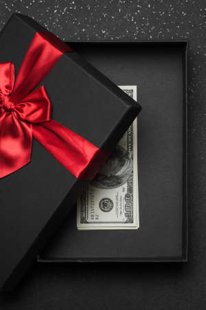 An open black gift box with a red ribbon and a large bow with money inside. Granite backgroundの写真素材