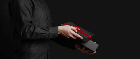 A guy in a black shirt holds an open gift box with a red bow. Gift in hand. Black background....
