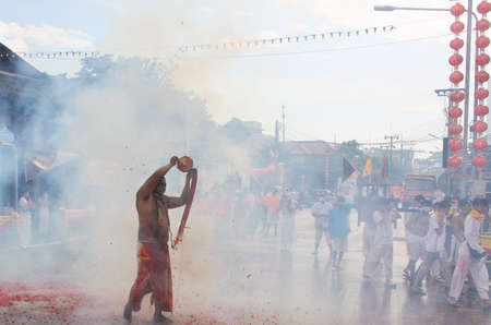 Phuket Town / Thailand - October 7, 2019: Nine Emperor Gods Festival or Phuket Vegetarian Festival parade, Thai Chinese devotee entranced man or Ma Song holding a long string of exploding firecrackersのeditorial素材