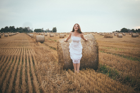 Beautiful Girl Running in the Field with a Bales of Hayの写真素材