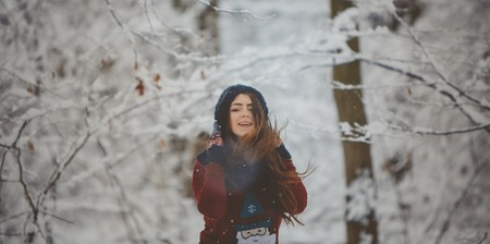 Woman on the background falling snow in winter forestの写真素材