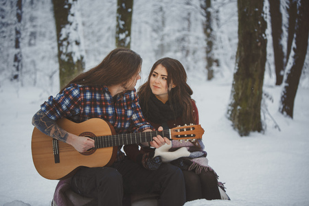 Man plays guitar to his girlfriend in winter forestの写真素材