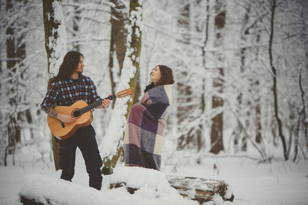 Man plays guitar to his girlfriend in winter forestの写真素材