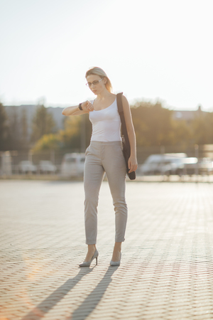 Business woman using a phone and clock while standing in outdoorの写真素材