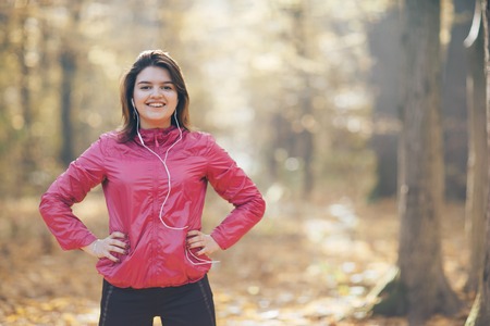 Portrait of a girl who trains and listens to music in the morning autumn parkの写真素材