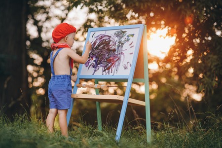 Little boy artist standing under the tree and drawing on the easel at parkの写真素材