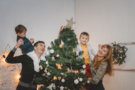 Parents and two son decorate the Christmas tree indoors. The morning before Xmas. Loving family close up.の写真素材