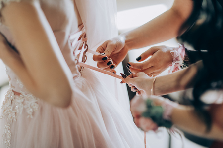 Bridesmaid preparing bride for the wedding day. Bridesmaid helps fasten a wedding dress the bride before the ceremony. Best wedding morningの写真素材
