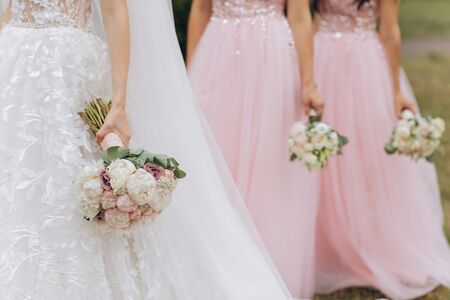 Row of bridesmaids with bouquets at wedding ceremony. Three bridesmaids holding wedding bouquets. Bride With Bridesmaids Outdoors At Weddingの写真素材