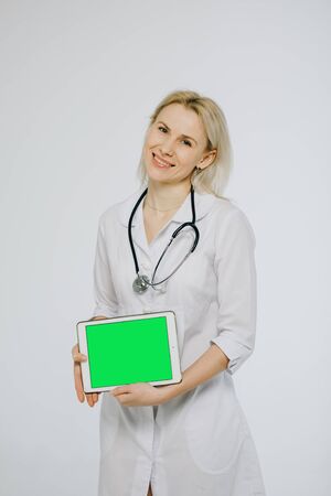 Caucasian female medical professional smiling happy on white background. Medical nurse doctor showing tablet pc computer green screen with copy space for your text or design.の写真素材