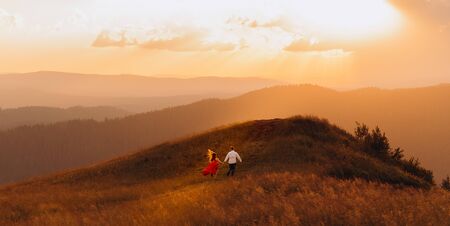 Silhouetted couple in love embrace and enjoy intimate moment together sky background sun shine light beams. Man and woman run along the road to the somewhere on the hill while sun shines over themの写真素材