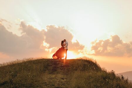 Happy couple stands in embrace and kisses each other on beautiful sunset in mountain.の写真素材