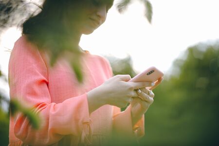 Woman using smart phone at outdoor and green nature background. Girl Hands holding smartphone. Woman Using Smartphone in Beautiful Green Parkの写真素材