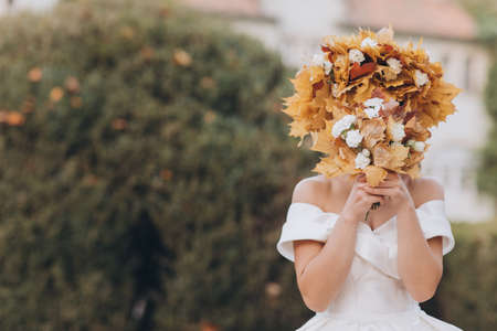 Brunette Bride in the Autumn Forest in a White Dress in a Wreath of Leaves. Brunette Bride with Wreath Leaves in her Hair. Look in a White Dress on a Background of Autumn Forest.の写真素材