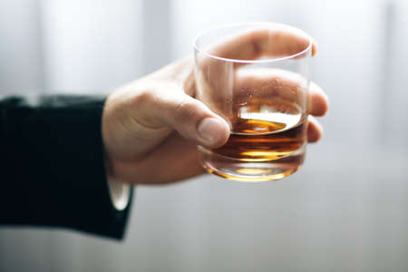 Mans hand holding glass of whiskey. Lonely man is addicted of alcoholの写真素材