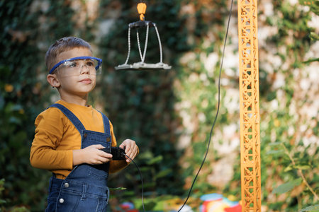 Portrait of little boy with remote control crane beam in an industrial warehouse. Little boy engineer builder worker is loading and unloading. Dreaming of future professionの写真素材