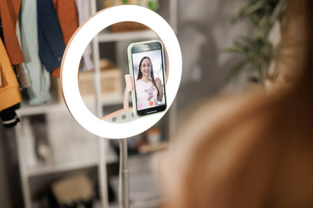 Beauty influencer filming tutorial at home. Young female blogger live streaming a broadcast online with ring light for a vlog channel. Recording a fun podcast for followers on social media.の写真素材