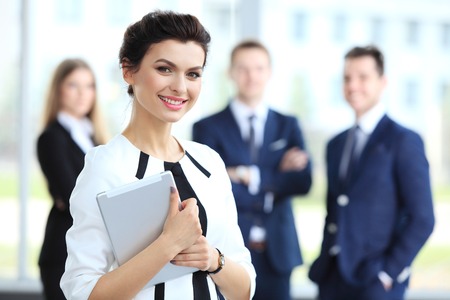 Business woman standing in foreground with a tablet in her hands her coworkers discussing business matters in the background Business woman standing in foreground with a tablet in her hands her coworkers discussing business matters in the background