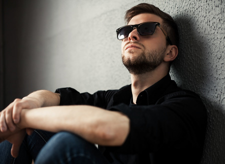 Young man in shirt siting with hands clasped against a wallの写真素材