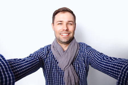I love selfie! Handsome young man in shirt holding camera and making selfie and smiling while standing against white backgroundの写真素材