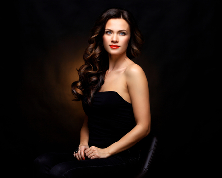 Beauty Model Woman with Long Brown Wavy Hair. Healthy Hair and Beautiful Professional Makeup. Red Lips and Smoky Eyes Make up. Gorgeous Glamour Lady Portraitの写真素材