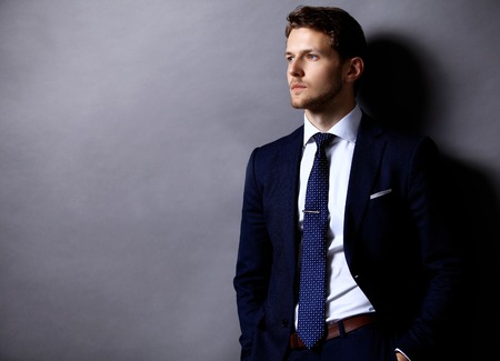 Cool young businessman standing on grey backgroundの写真素材
