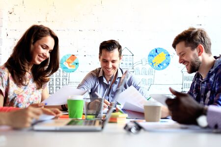 Making great decisions. Young beautiful woman gesturing and discussing something with smile while her coworkers listening to her sitting at the office tableの写真素材
