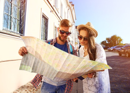 Happy couple walking outdoors sightseeing and holding a mapの写真素材