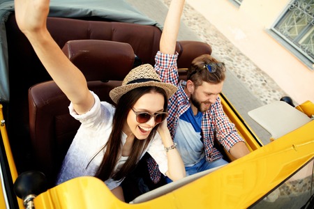 Happy to travel together. Joyful young couple smiling while riding in their convertibleの写真素材