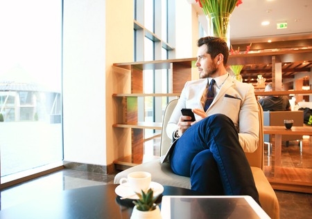 Portrait of handsome successful man drink coffee sitting in coffee shop, business man having breakfast at hotel lobbyの写真素材