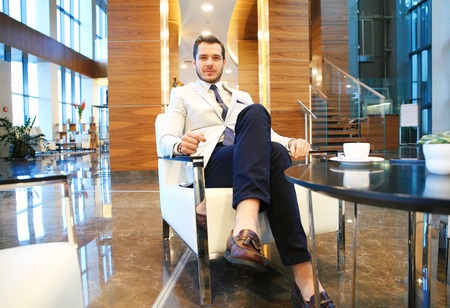 Portrait of happy young businessman sitting on sofa in hotel lobbyの写真素材
