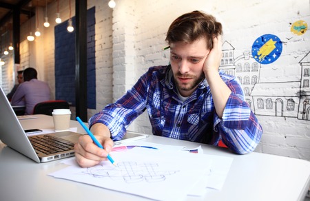 Photo young and talente finance manager working with new project. Handsome man working from his home office. Analyze business plans on laptop. Blurred background, film effectの写真素材