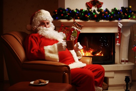 Santa Claus having a rest in a comfortable chair near the fireplace at home.の写真素材