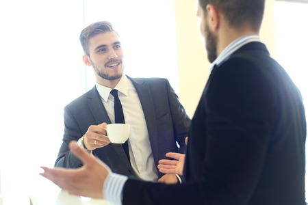 Image of young businessman with cup of coffee communicating with his colleague.の写真素材