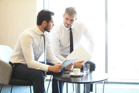 Image of two young businessmen using touchpad at meeting.の写真素材